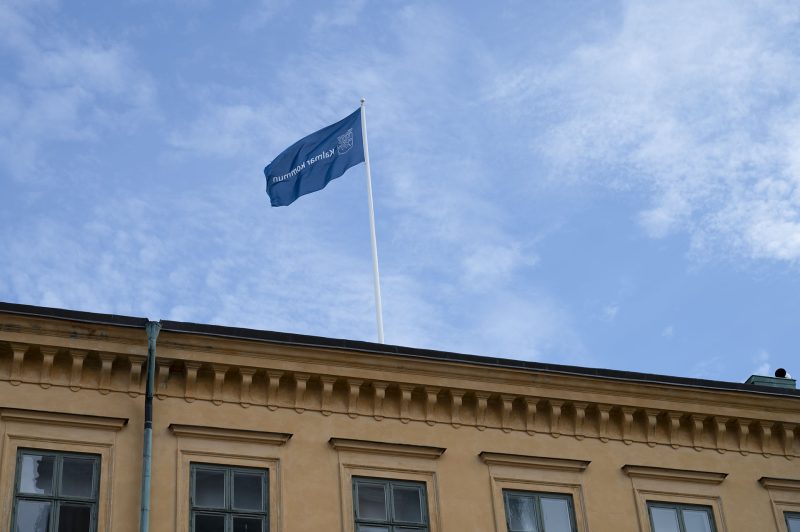 En blå Kalmar kommun flagga vajar på den blå himlen