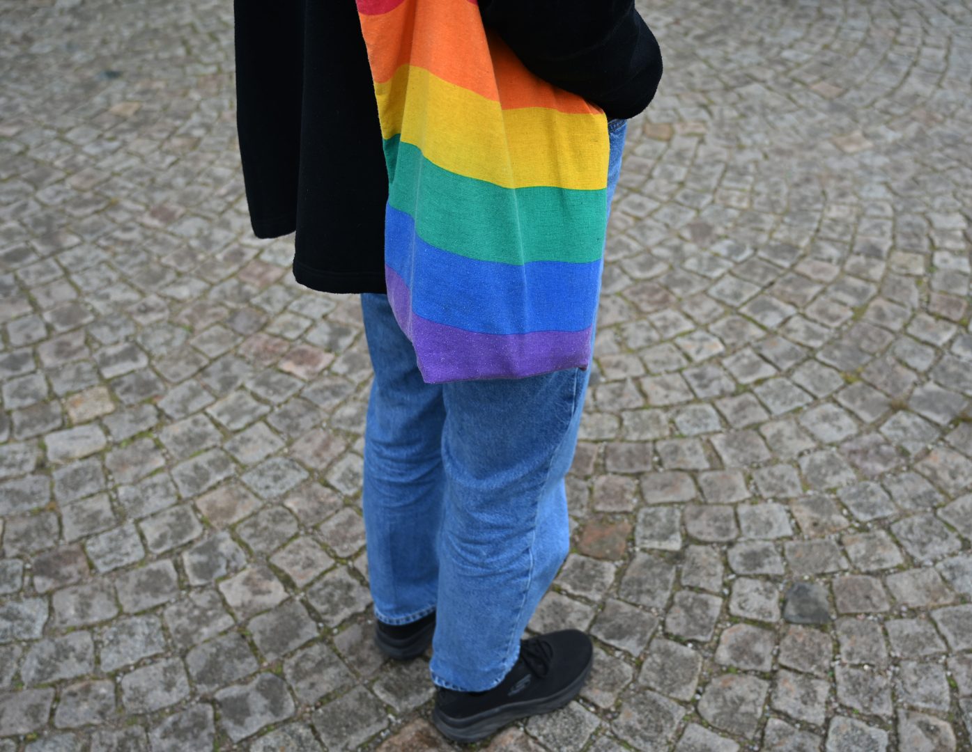 Person med tygpåse i regnbågens alla färger står utomhus.