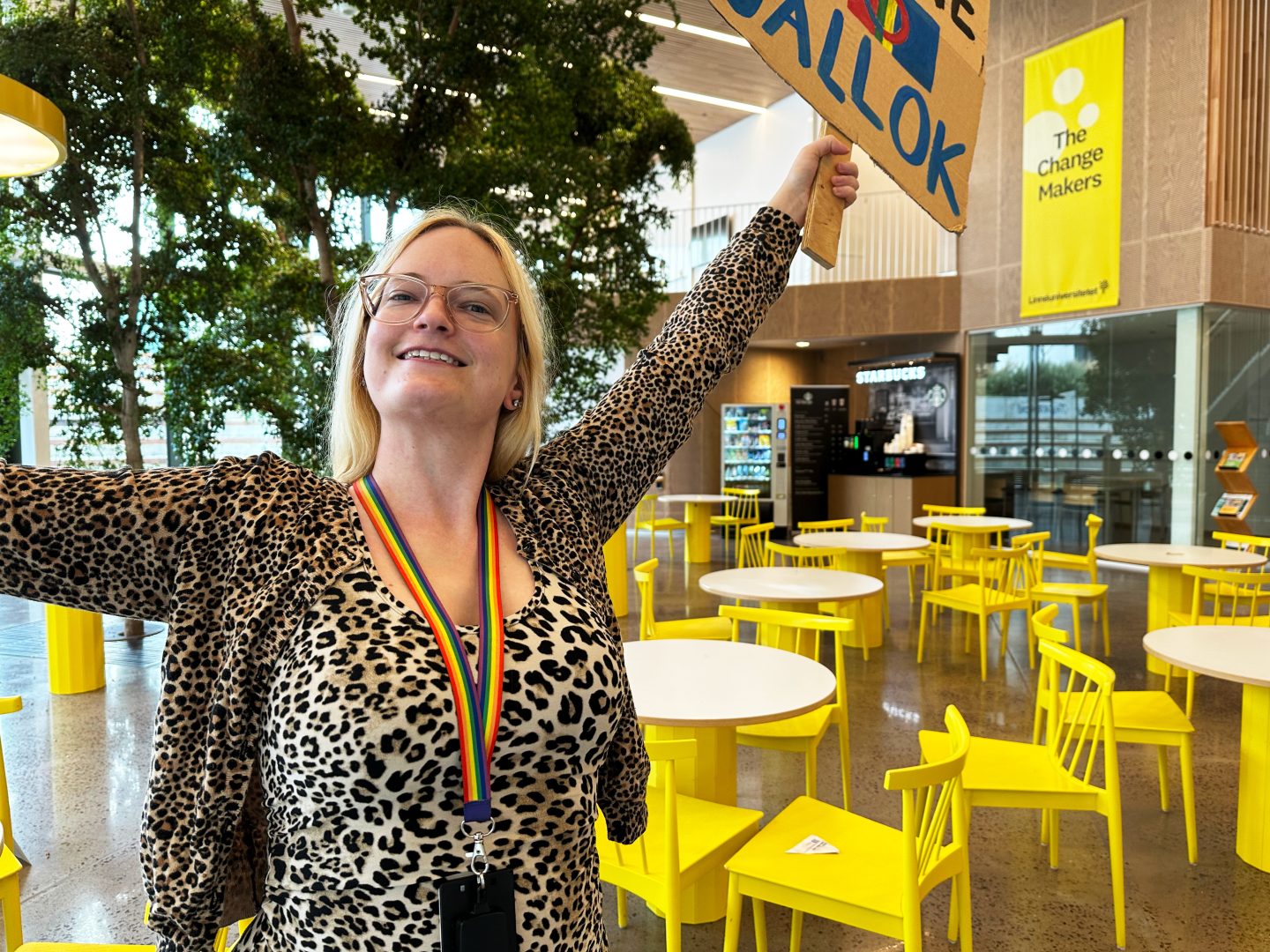 Ida krogsgaard står med ett stort leende på läpparna medan hon håller upp skyltar som fokuserar på klimataktivism.