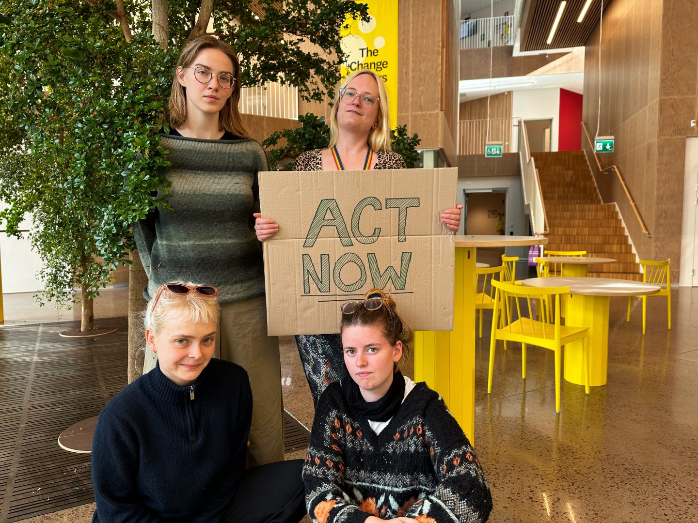 Klimataktivister står i byggnaden radix och tittar in i kameran. Ida Krogsgaard, som står uppe till höger, håller i en skylt med texten "act now".