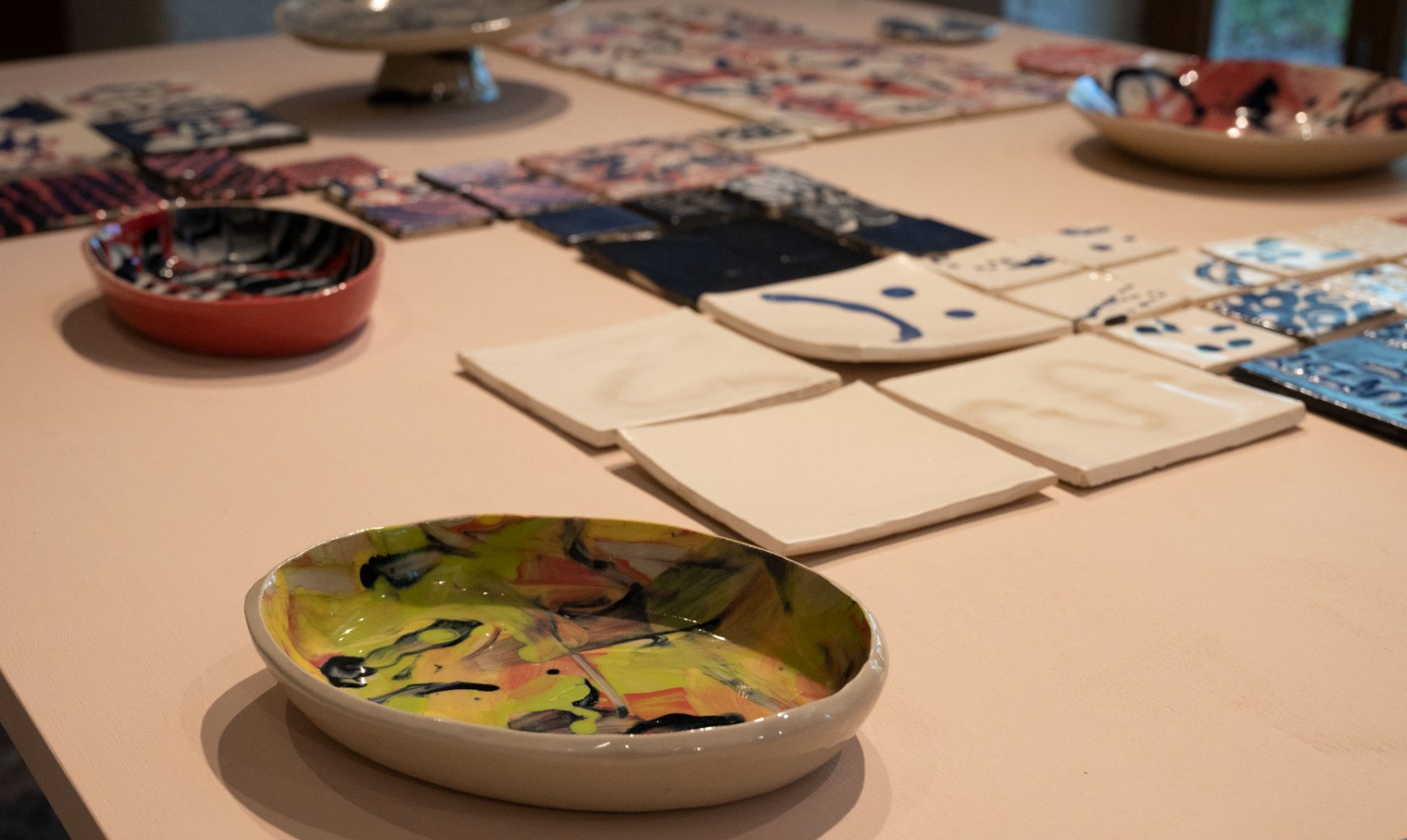 På ett bord ligger ett större antal färgglatt glaserade keramikobjekt.