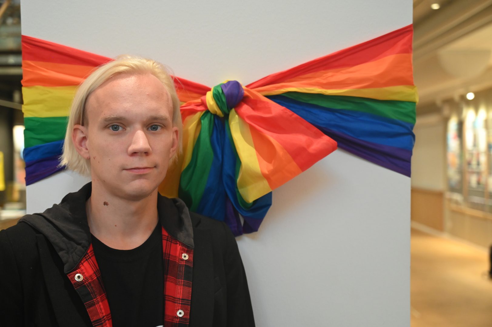 En person står inne på Kalmar Stadsbibliotek. Bakom sig har hon en prideflagga.