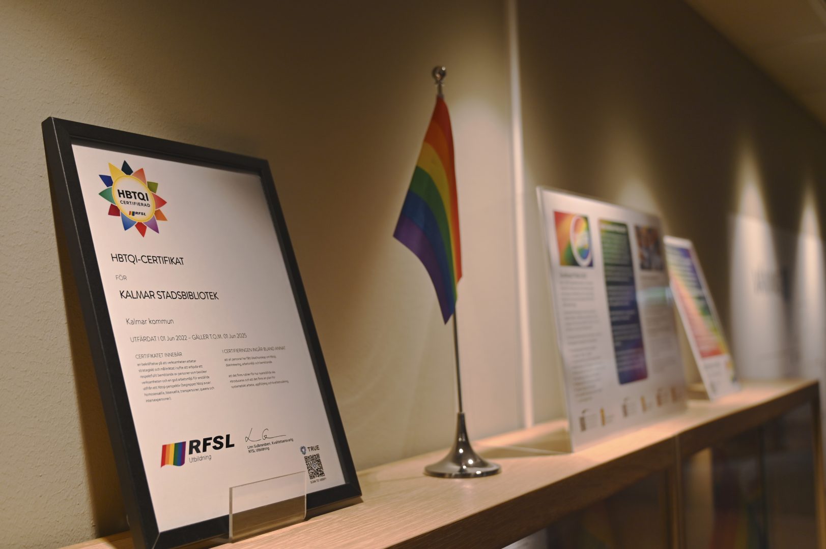 Olika tavlor och en prideflagga står upprade på en hylla.