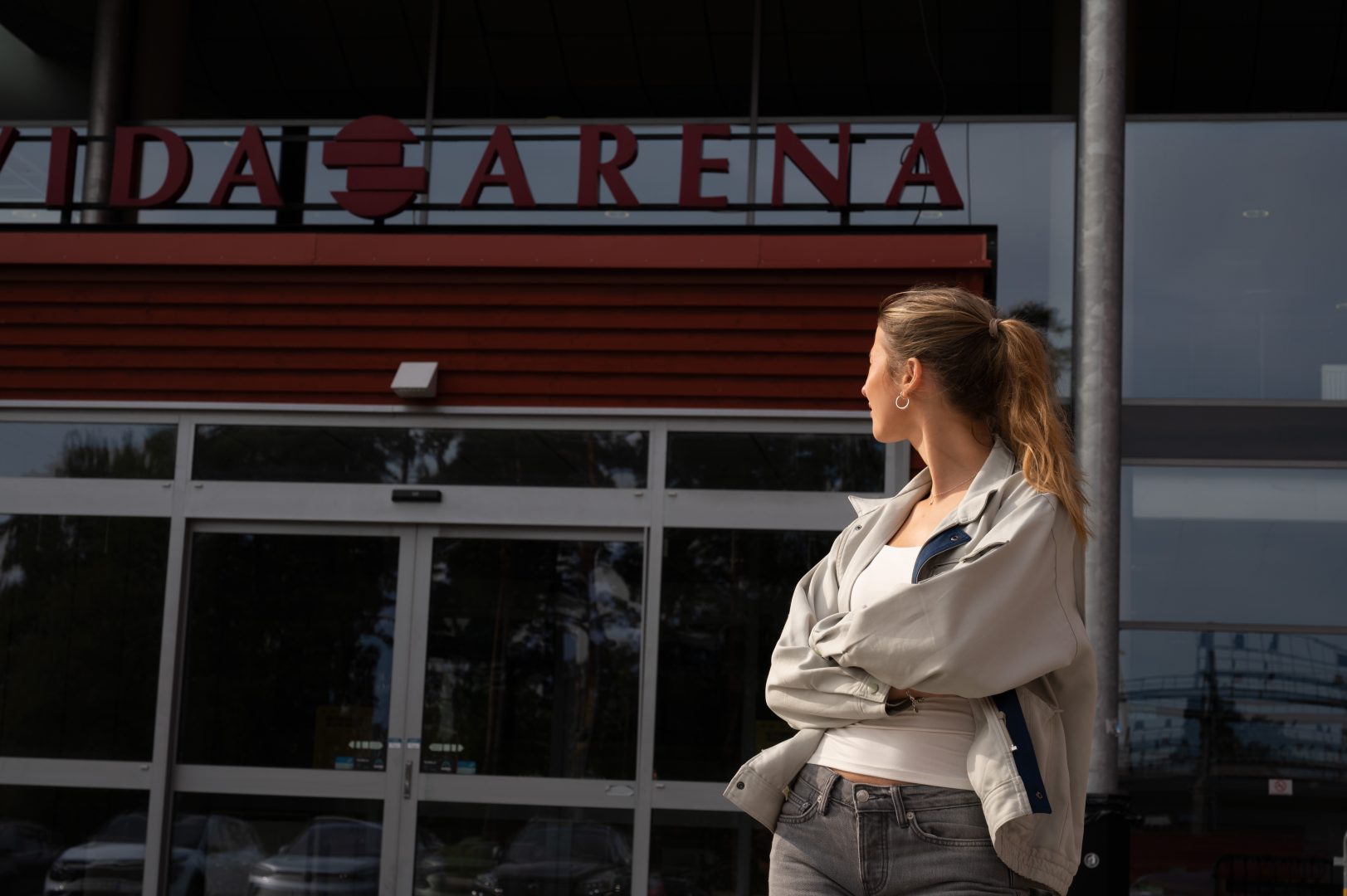 Reporten står framför Vida Arenas entré och tittar mot dörren. hon är placerad på höger sida och har armarna i kors.