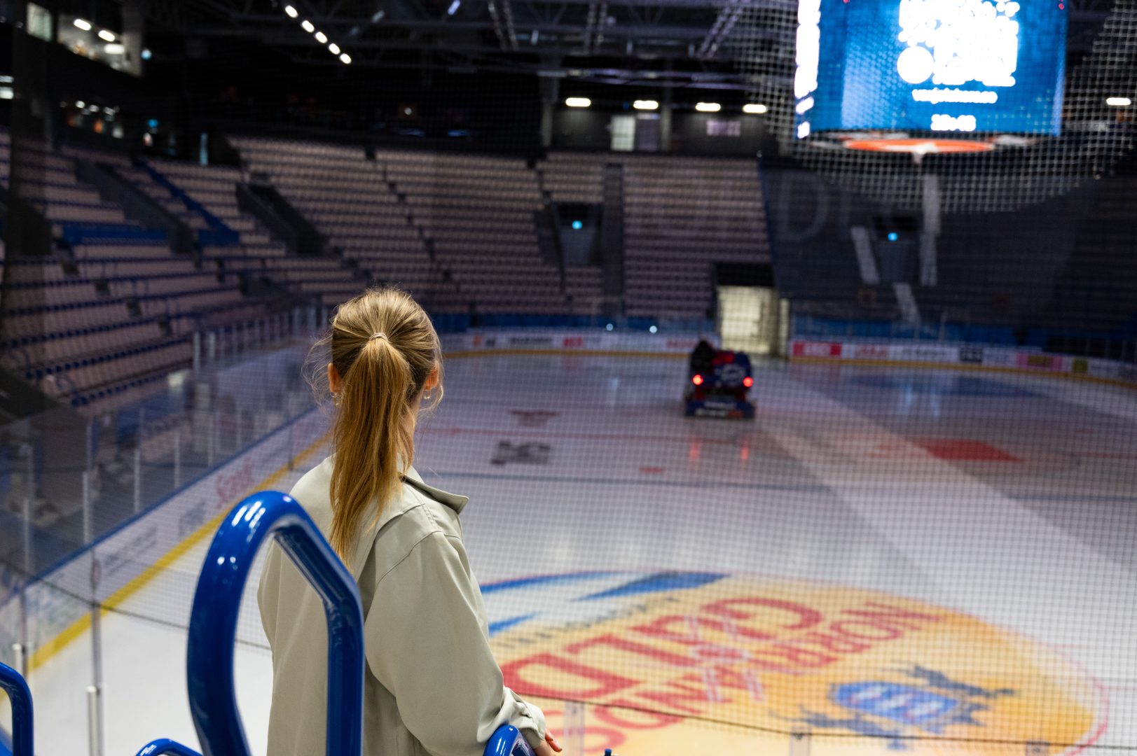 Reporten står till vänster i bilden. Hon tittar ut över arenan och framför henne är det en hockeyrink.