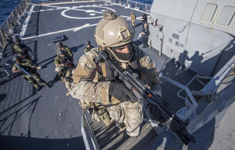 Grönklädd militär med vapen går upp för en trappa.