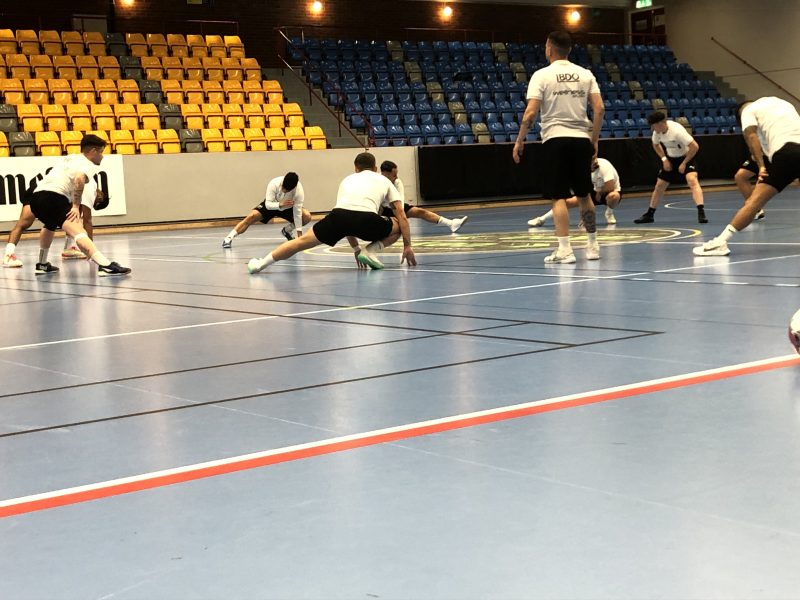 Spelarna i FC Kalmar stretchar inför en lugn träning. De tränar med sin vita tröjor och står i en ring där de gör sig redo.