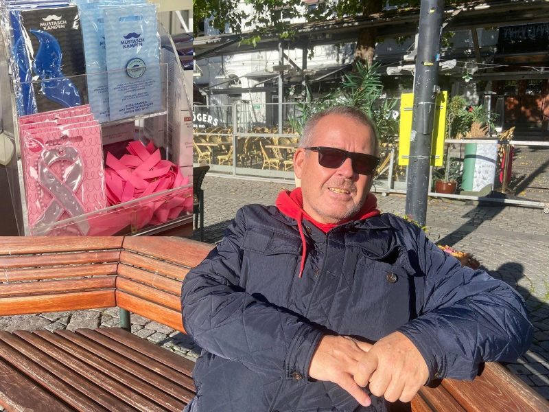 Tage Sjöström som sitter vid en bänk med solglasögon på. I hörnet finns en bild på rosa band i en butik.