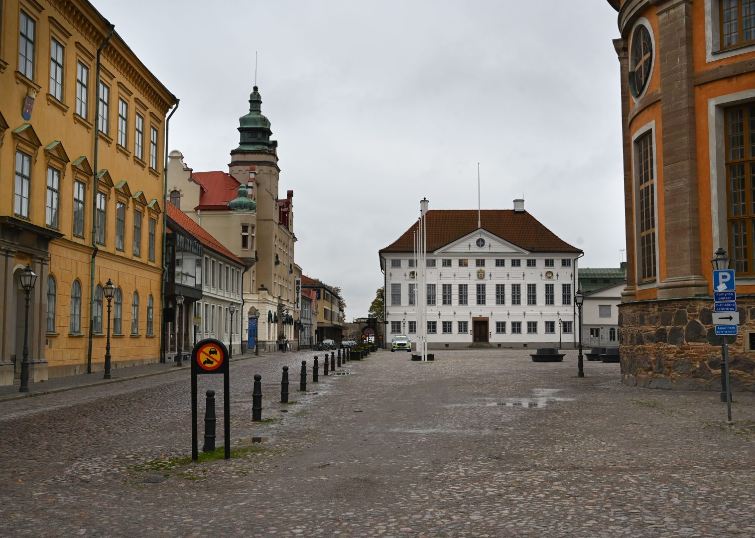 Färgfotografi på ett torg med en väg och byggnader i bakgrunden.
