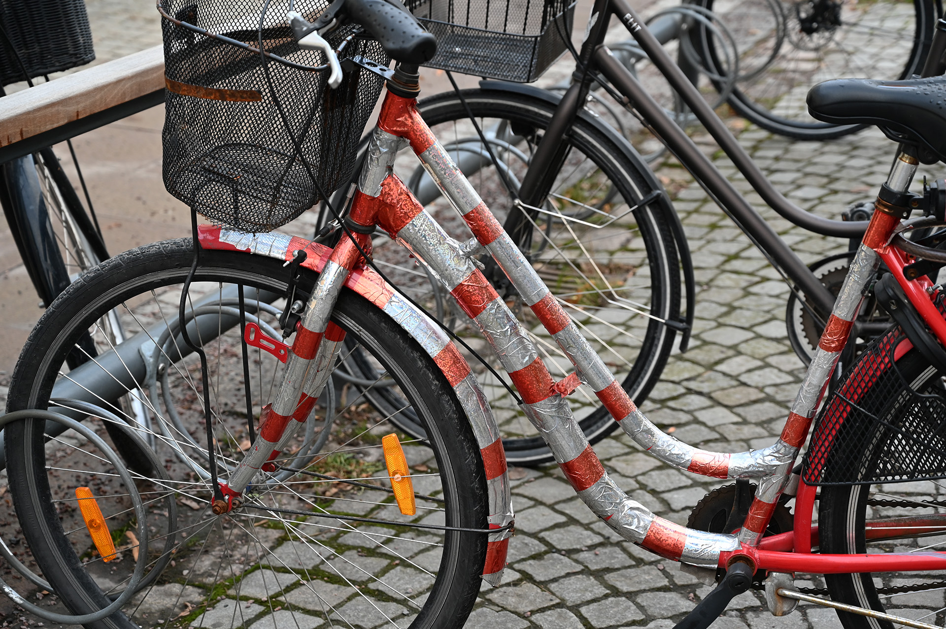 En cykel står parkerad i ett cykelställ, inklädd i något som liknar ett polkagrismönster i ramen.