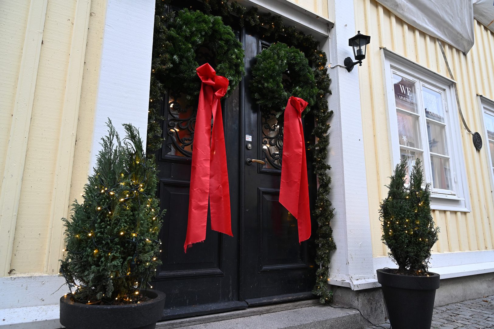 En svart dörr med grankransar och röda rosetter.