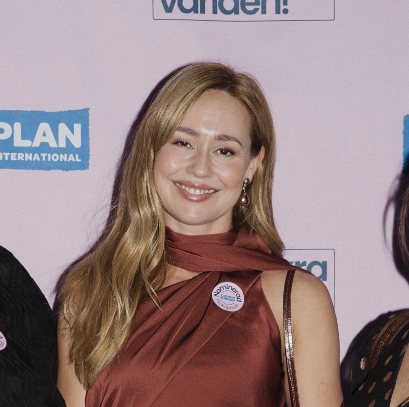 Porträtt av Charlotte Walden, Kvinnojourens projektledare, som ler mot kameran. Hon har långt ljust hår och bär en vinröd klänning med en knapp som visar att hon är nominerad. Fotot är taget vid ett prisutdelningen för Plan Internationals Flickapris.