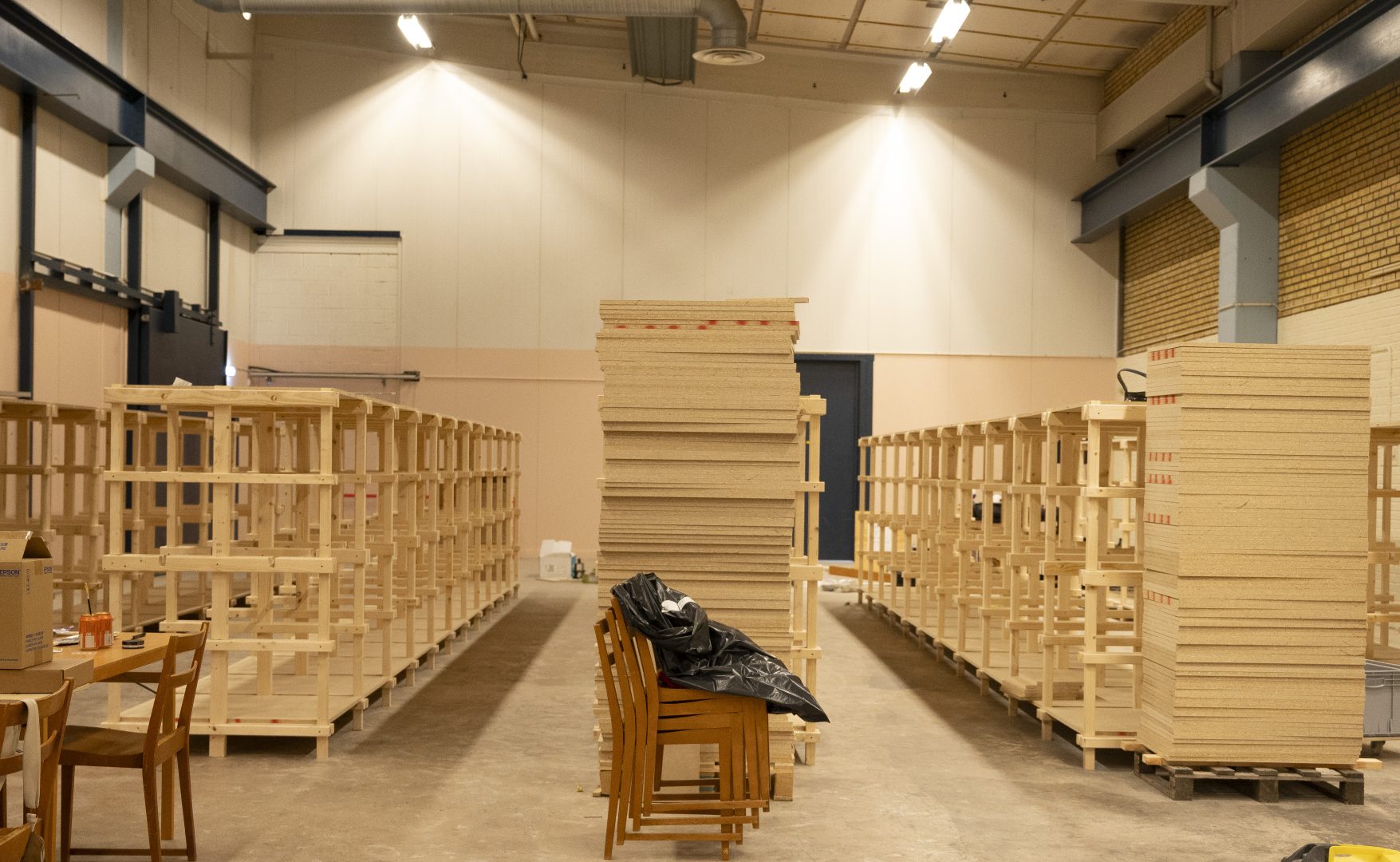 Flera hyllor i ljust trä står på rad i en industrilokal.