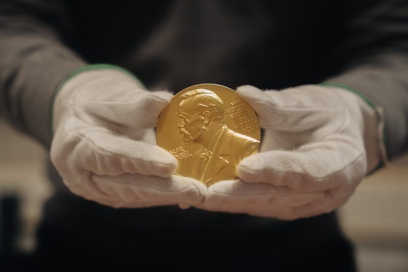 Händer som håller i ett mynt med Alfred Nobel på. (Nobelpriset)