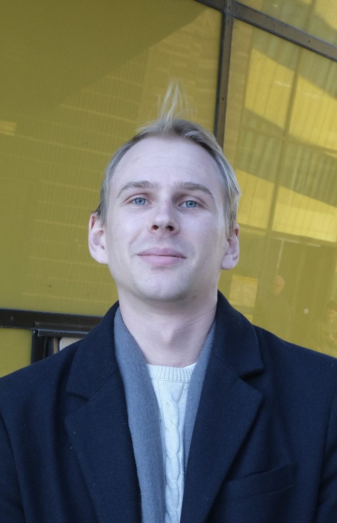 Erik Daxberg som står framför en gul byggnad och kollar in i kameran