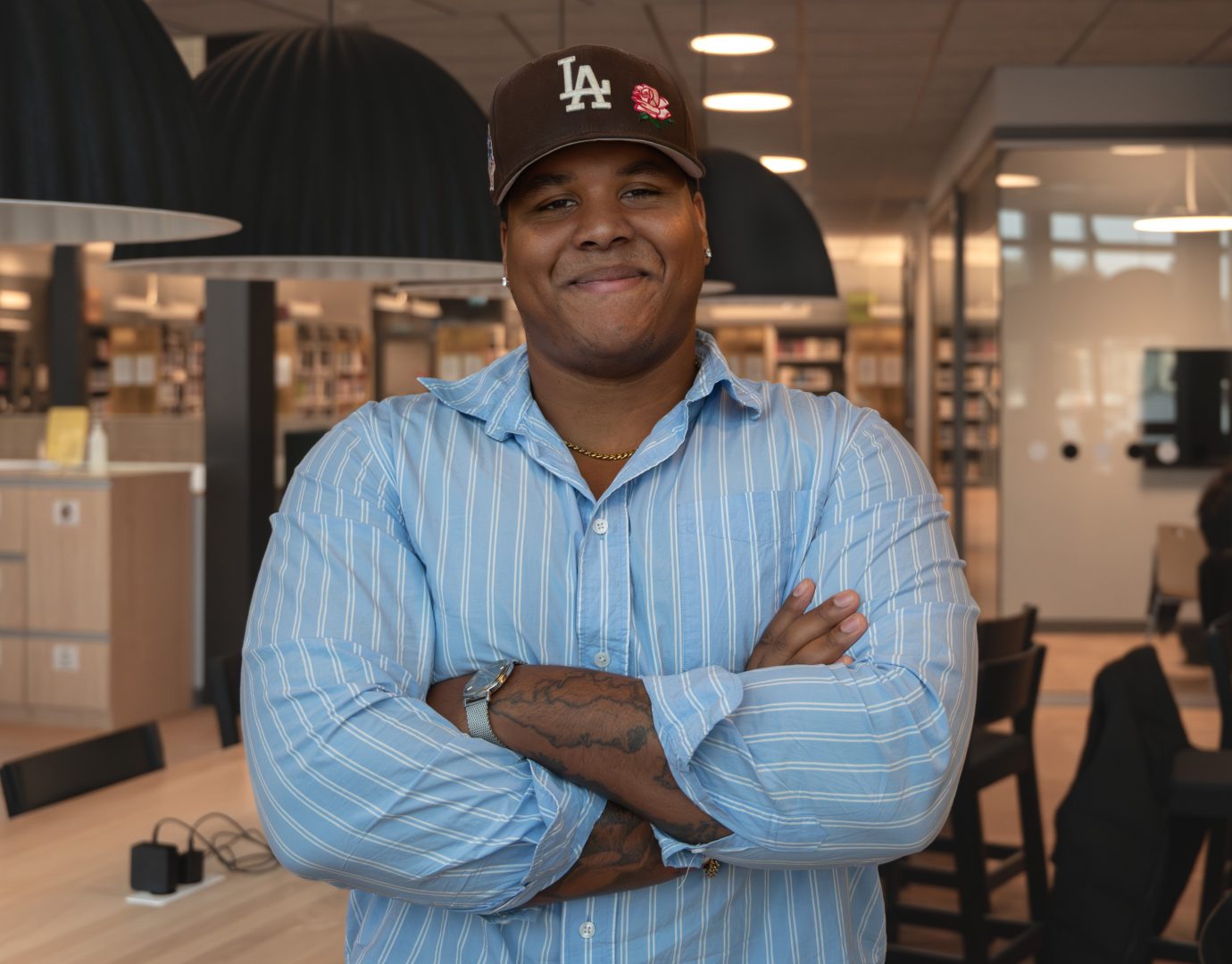 Henry Zetterlind står framför kameran och ler med armarna i kors. Han står i biblioteket och i bakgrunden ser man stolar och bord.