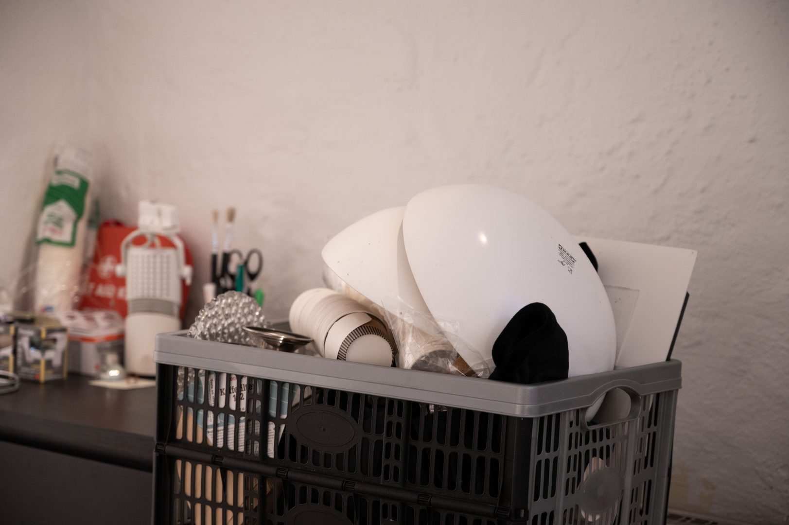 På bilden syns en plastkorg som står på en diskbänk. Ur korgen sticker det upp vita tallrikar, muggar och andra köksredskap.