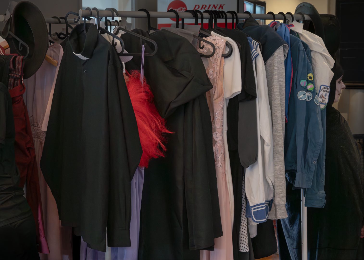 På en grå klädstång hänger ett tiotal kostymer. Bredvid klädstången till höger står en kvinna utklädd till nunna. Hon har svarta kläder och är vitmålad i ansiktet