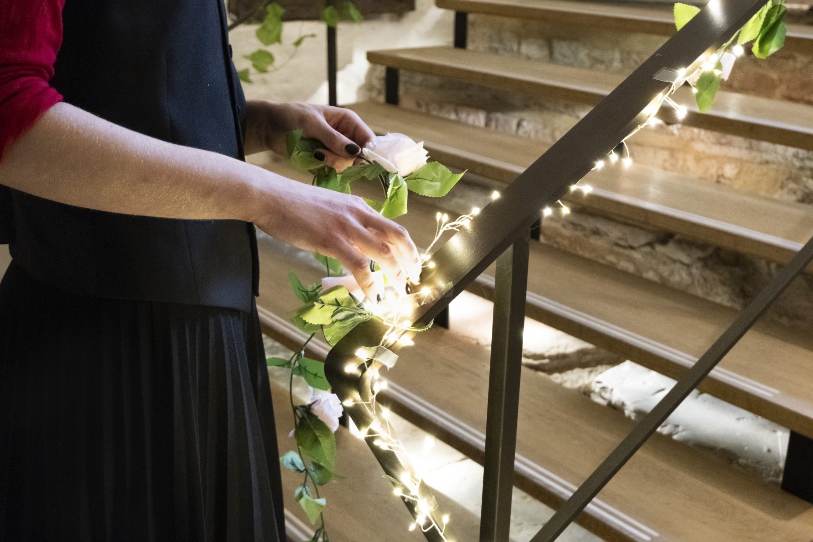 En person som står och virar en ljusslinga runt ett räcke.