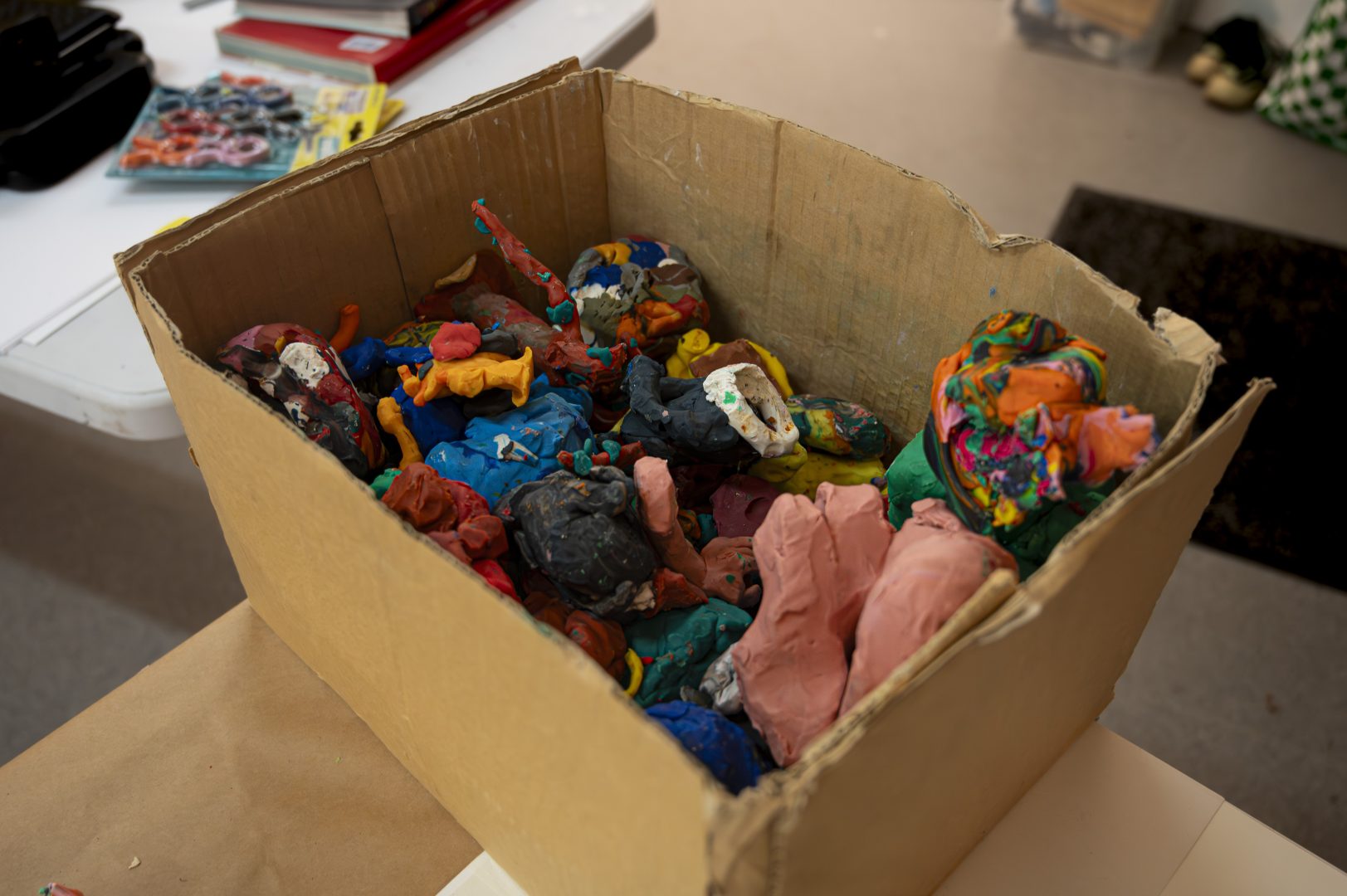 Första bilden visar en öppen kartong fylld med färgglada, leriga skapelser, konstverk eller modeller gjorda av lera.