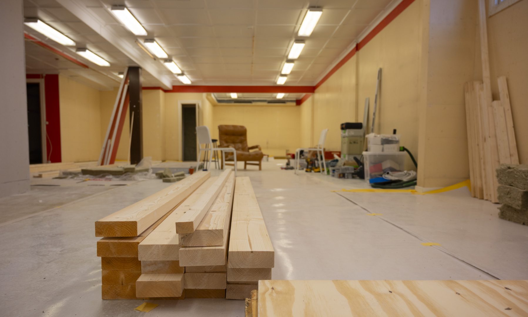 En stor lokal med virke på golvet. Rummet är under renovering, med gula väggar och en brun läderfåtölj i mitten av rummet. Längs väggarna står det olika renoveringsverktyg.