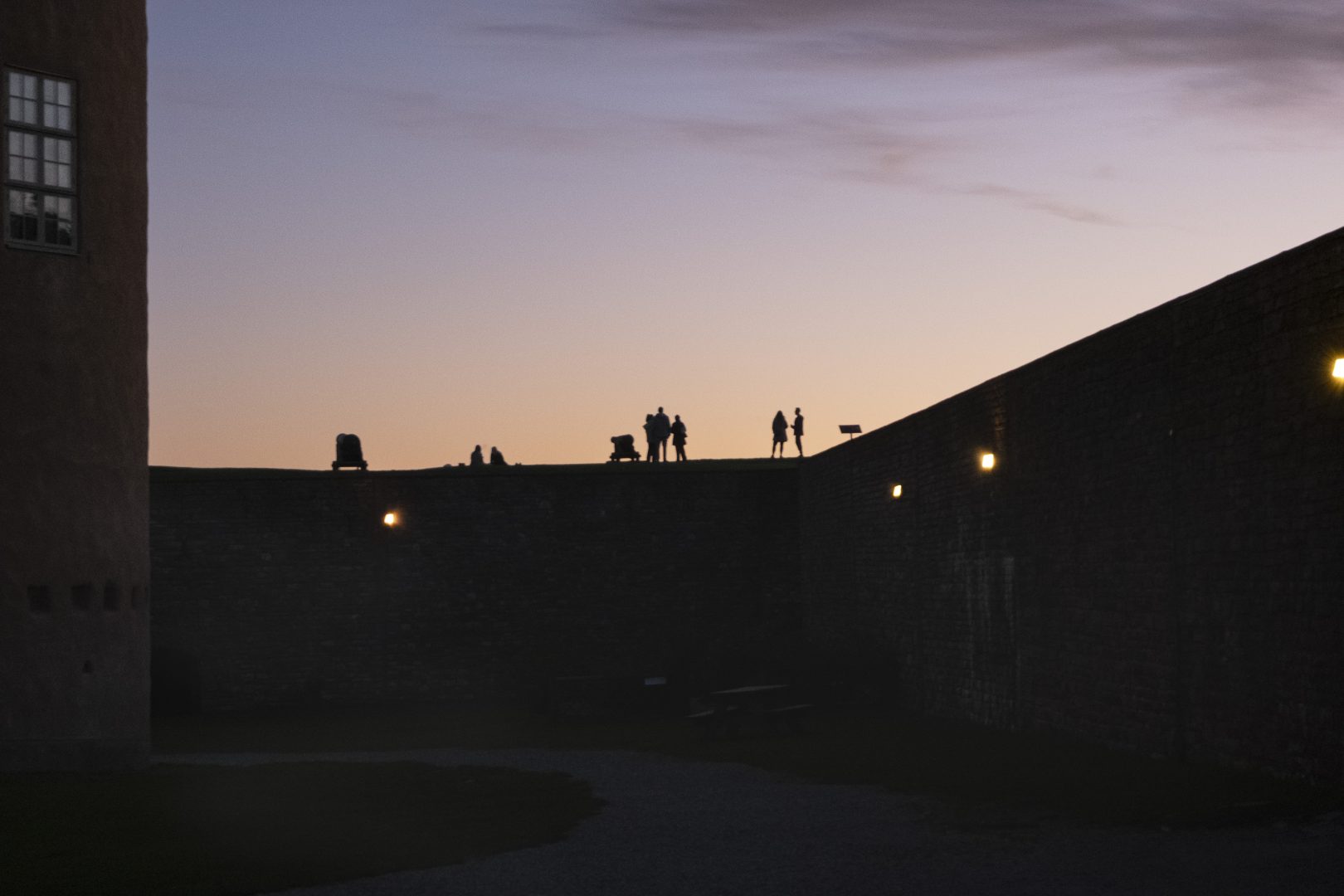 Människor som står uppe på slottsmuren mot solnedgången.