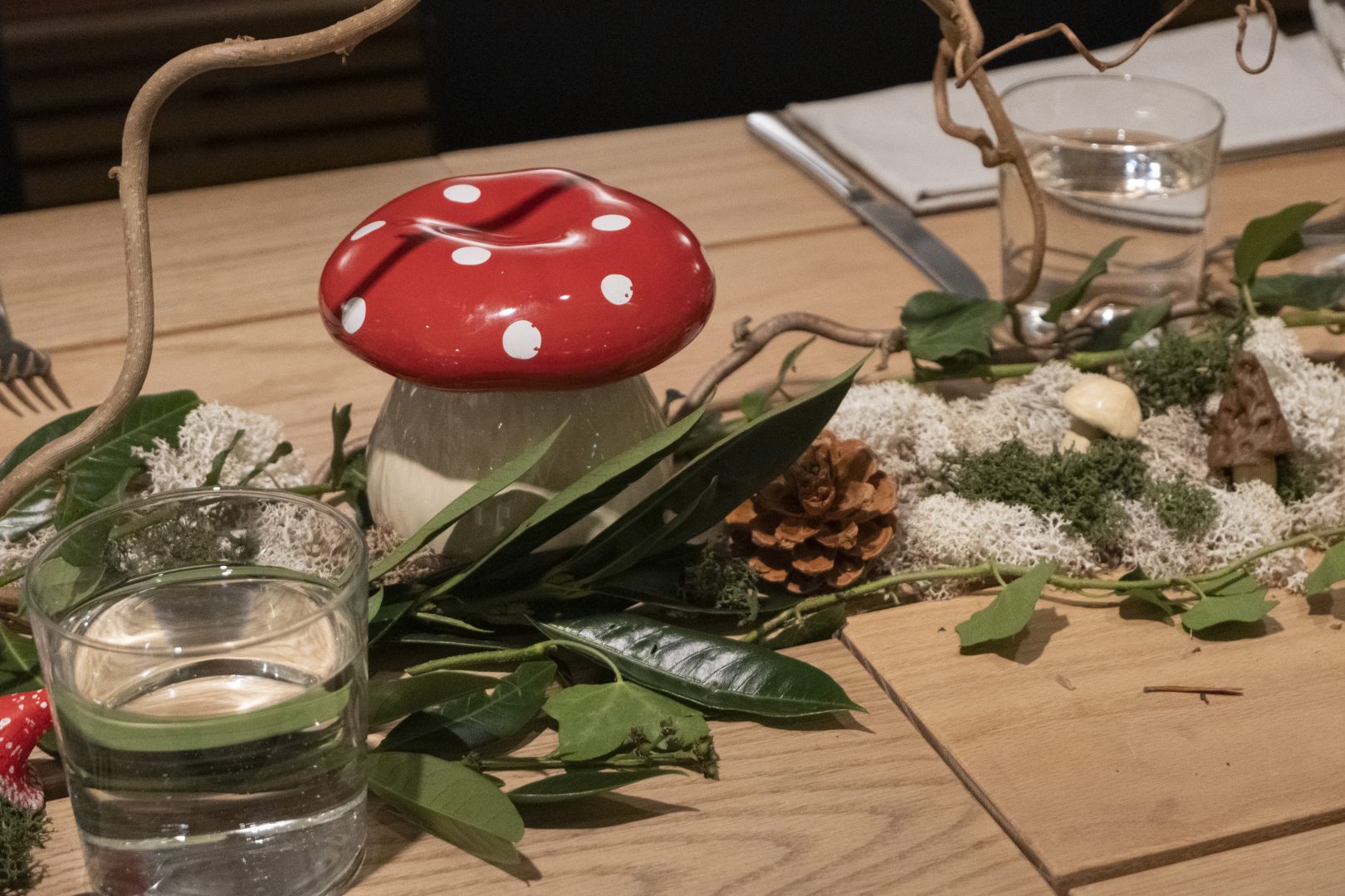 En röd fejk svamp som står på ett träbord med löv och kottar som dekoration.