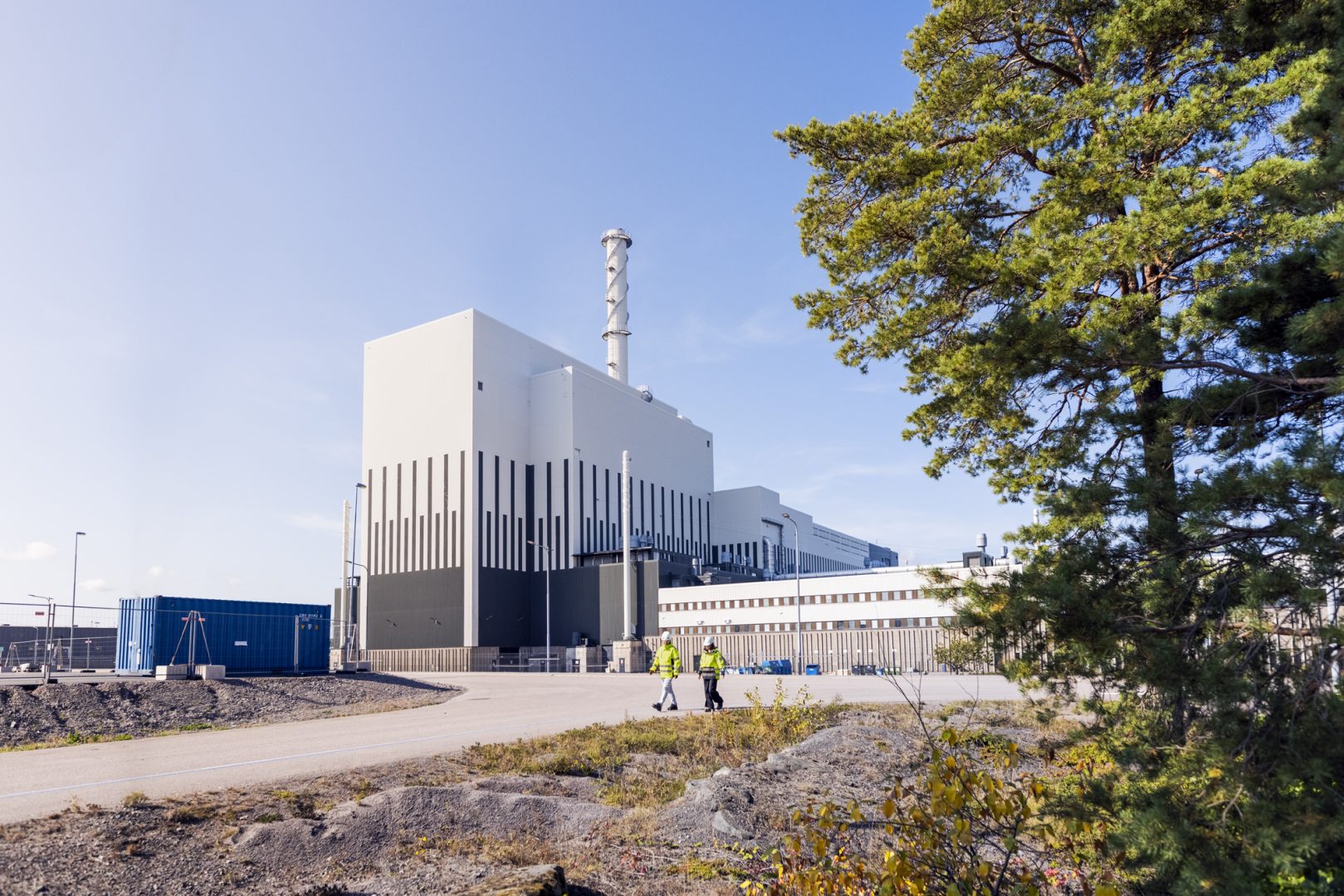 bild på ett vitt kärnkraftverk. Ett grönt träd finns på höger sida i bilden.