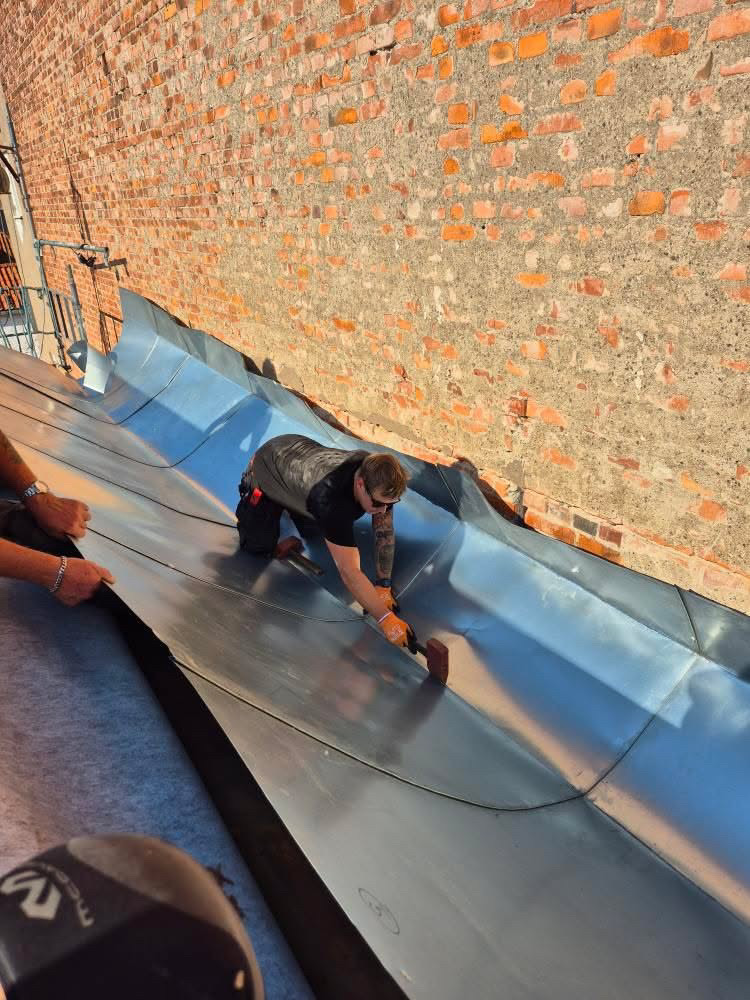 En plåtslagare hamrar plåt på ett tak.