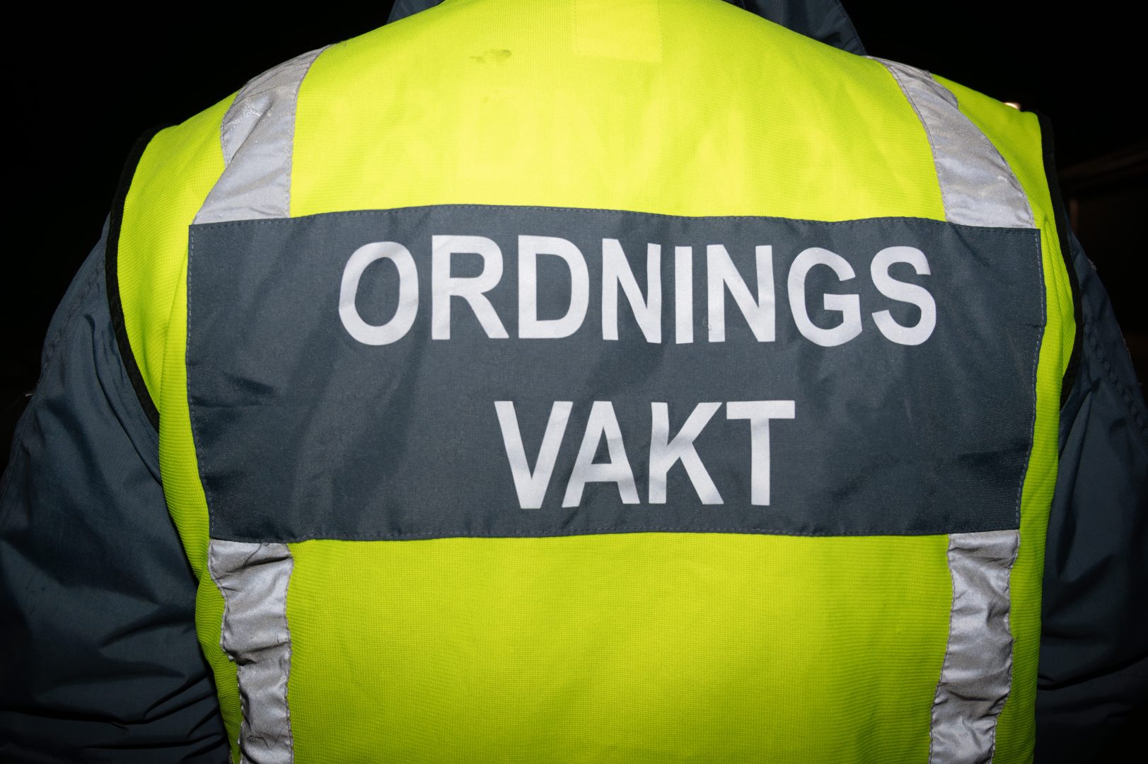 Ryggen på en ordningsvakt. Han har en gul reflexväst på sig med texten "ordningsvakt".
