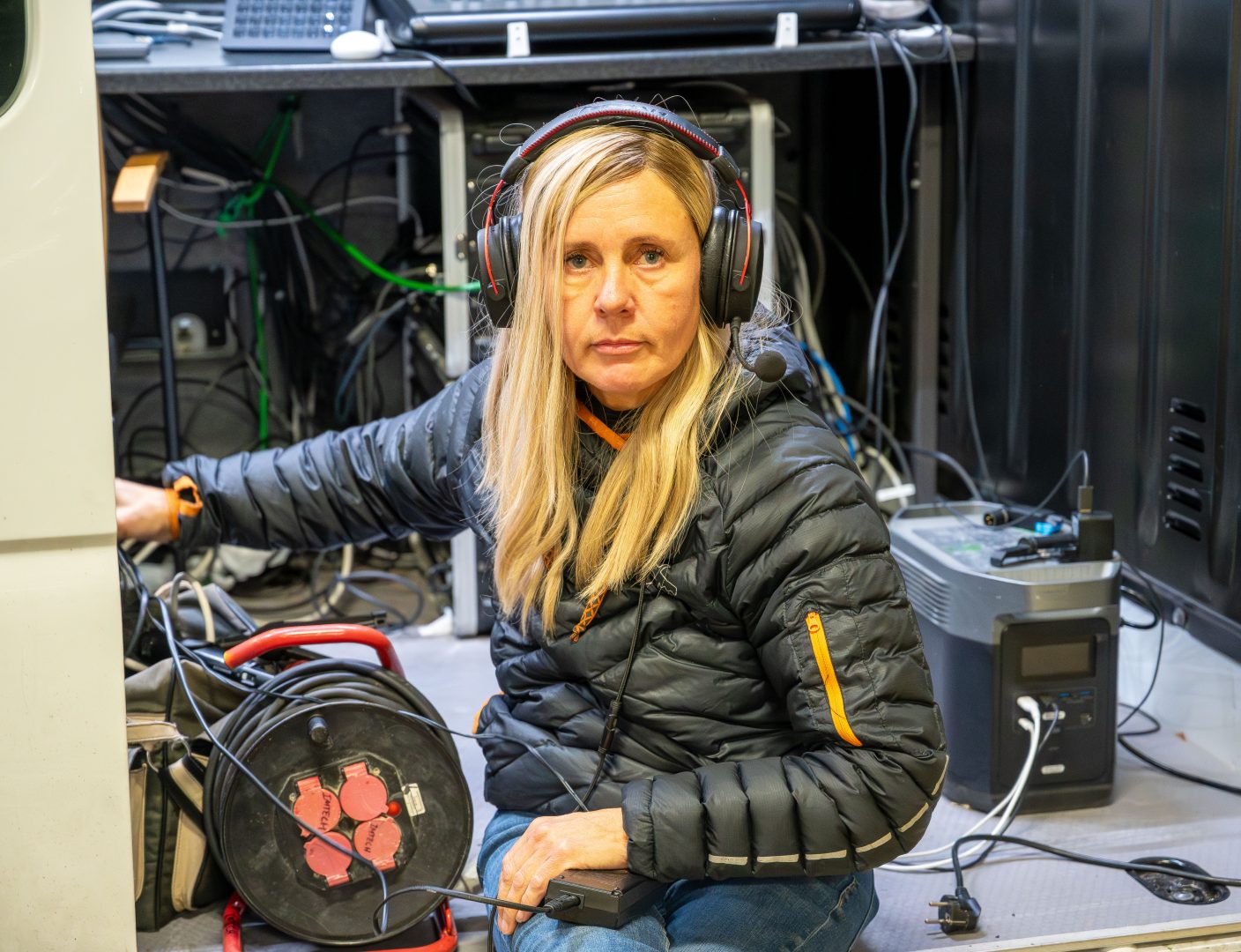 Johanna Eriksson sitter i dörren på en minibuss med utdragen sladd i handen och hörlurar på huvudet.