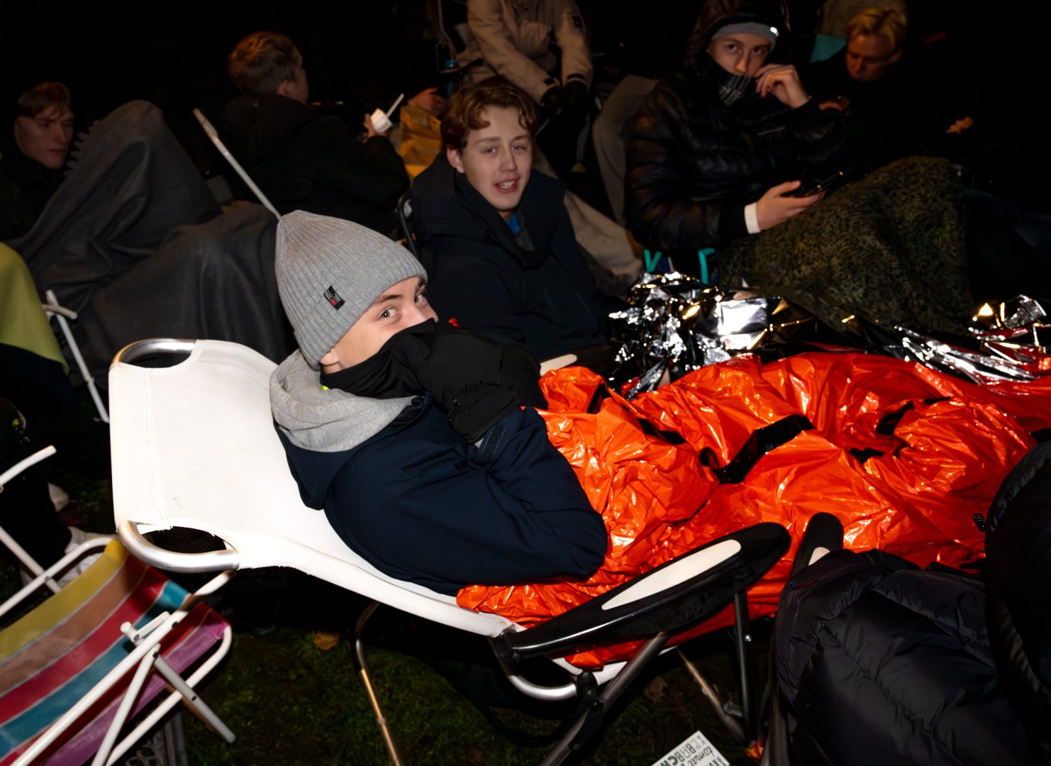 Edvin Eriksson sitter utomhus på en brassestol mitt i natten. Han har plast runt sig som en filt.