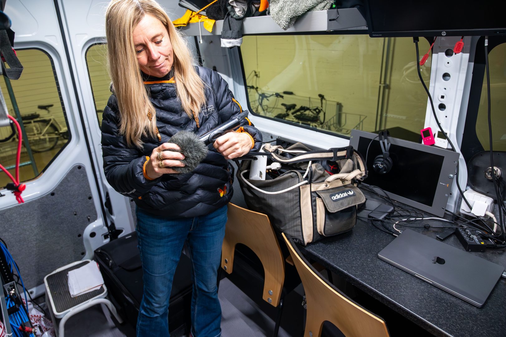 Johanna Eriksson står i bussen och pysslar med utrustning. En mikrofon och en väska med sladdar.