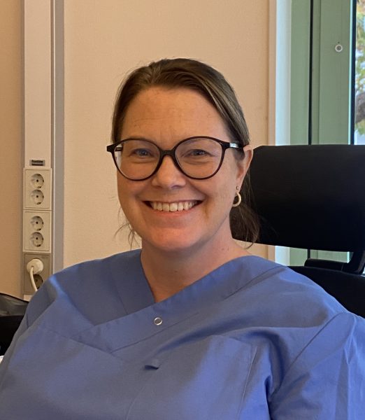 en kvinna sitter framför ett fönster och ler mot kameran