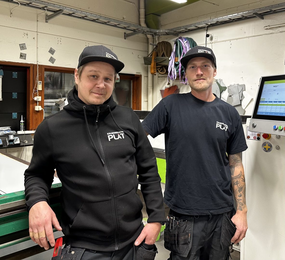 Chefen och medarbetare står och ler mot kameran på sin arbetsplats. 