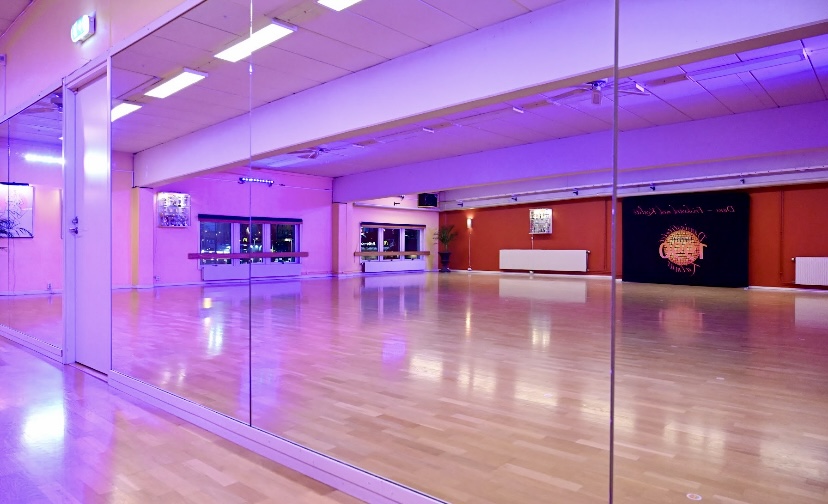 Bilden visar en stor dansal med trägolv och en stor spegelvägg.