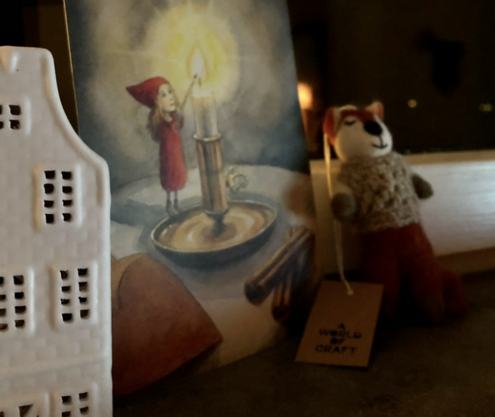 en bild på ett adventsljus som tänds och nåpgra juldekorationer.