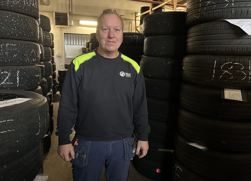 En man står i arbetskläder framför uppradade däck.