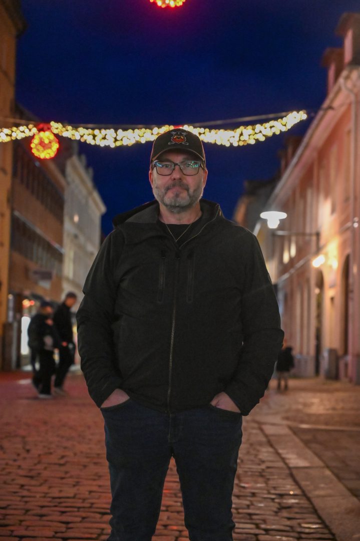 En helbild på Sam Cansund med julbelysning i bakgrunden i utomhusmiljö