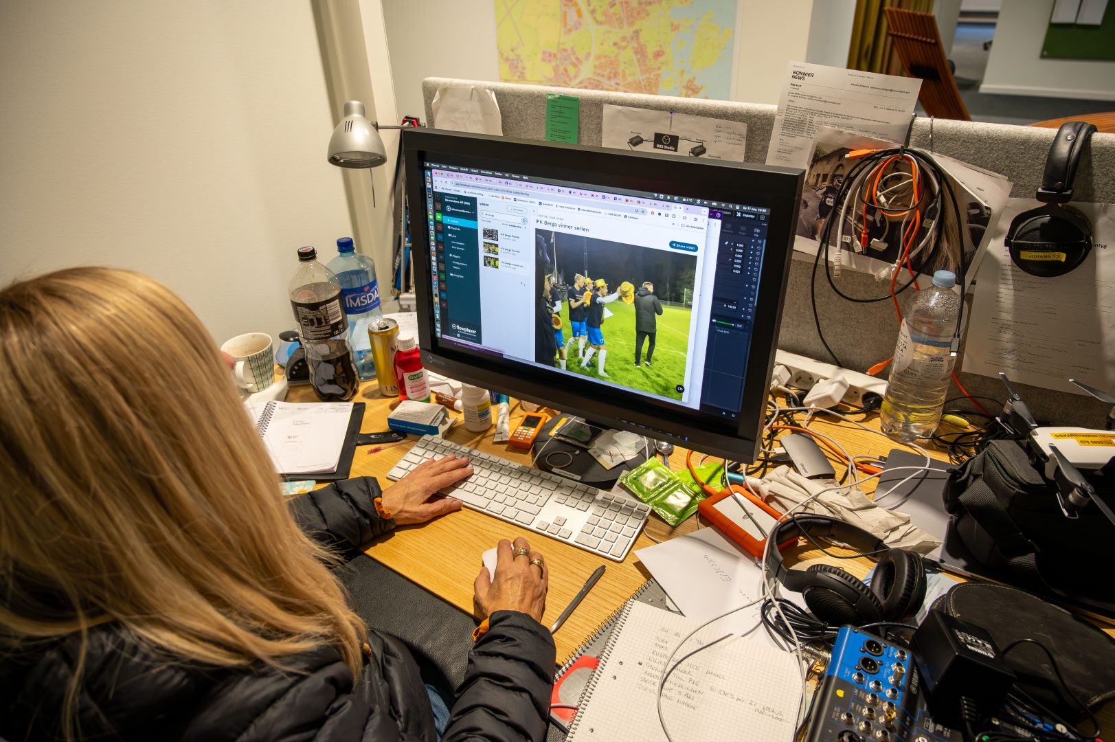 Johanna Eriksson sitter vi sitt skrivbord. Skrivbordet är stökigt, man kan tillexempel se burkar, flaskor och hörlurar.