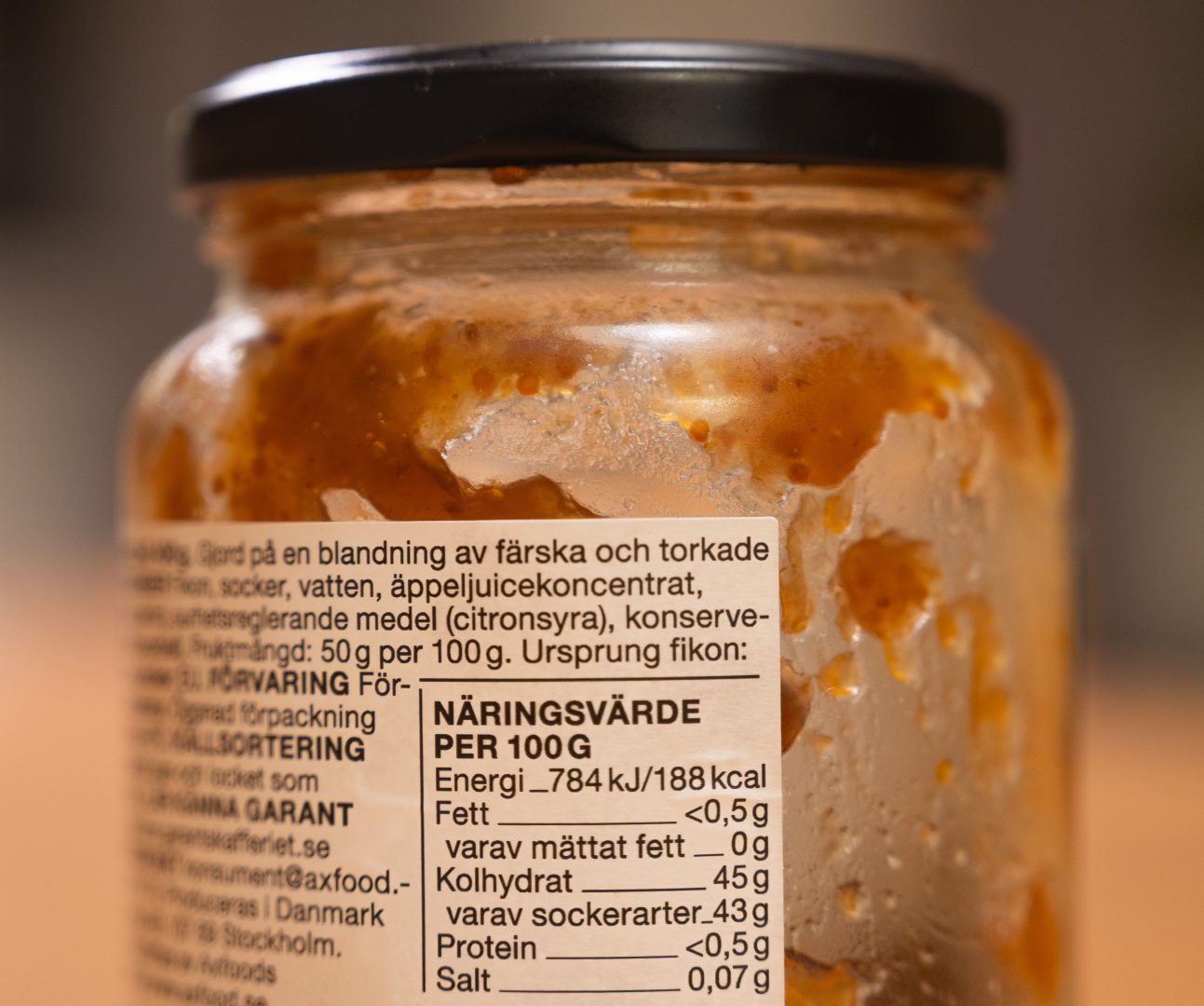 Närbild av en glasburk med brunaktig sylt där etiketten med ingredienslista och näringsvärde per 100 gram är i fokus. Texten visar bland annat energi, fett och sockerarter.