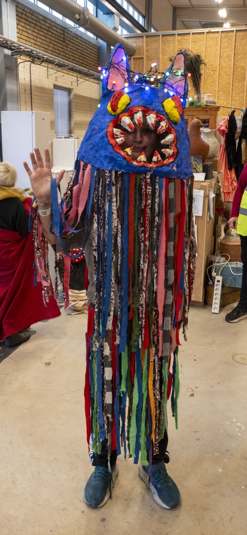 En elva årig kille står och vinkar mot kamera med sin egen gjord och färgglad kostym.