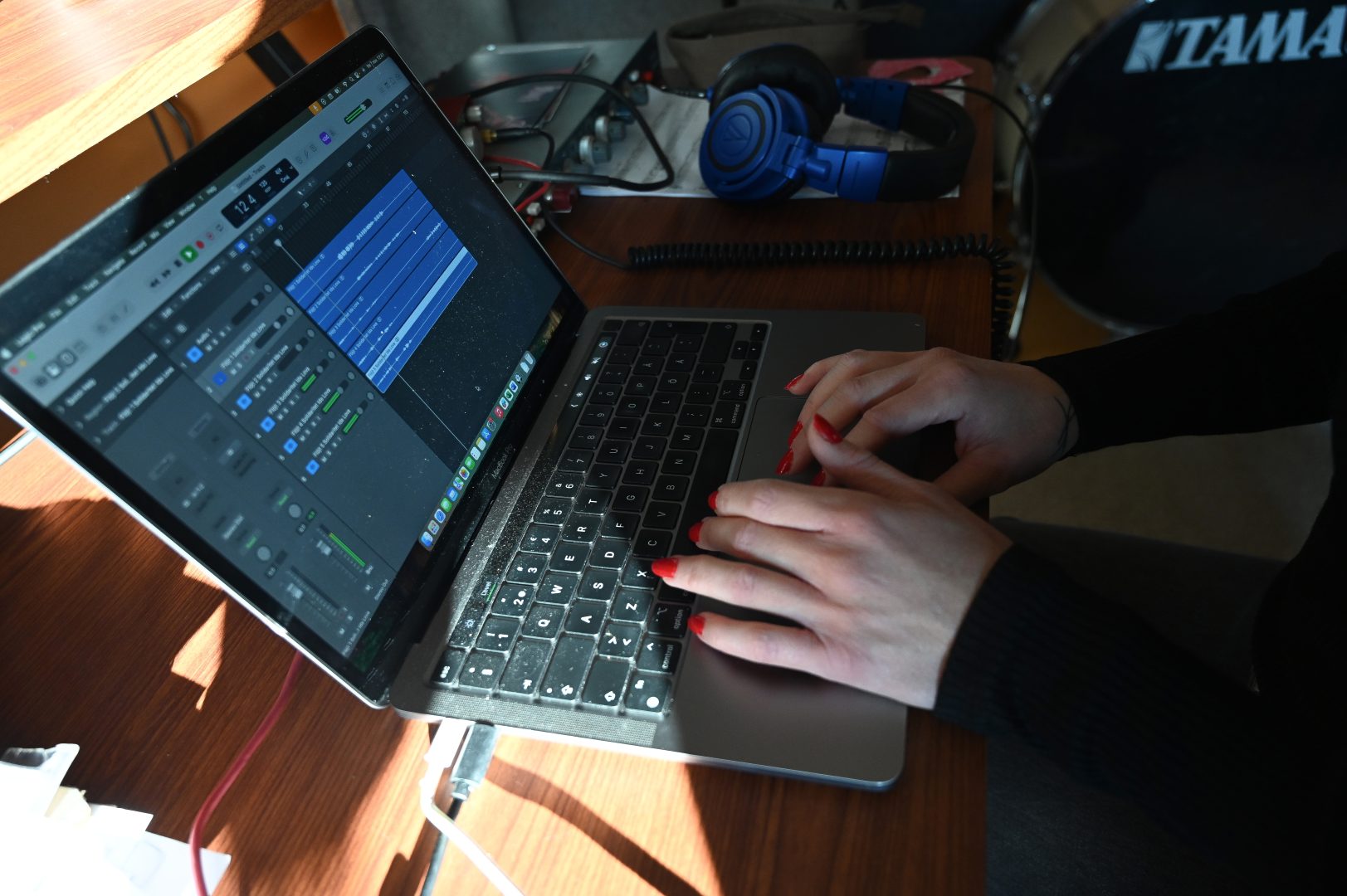 närbild på händer på en dator. Personen har rött nagellack på fingrarna. Datorn har ett program för musikproduktion uppe. 
