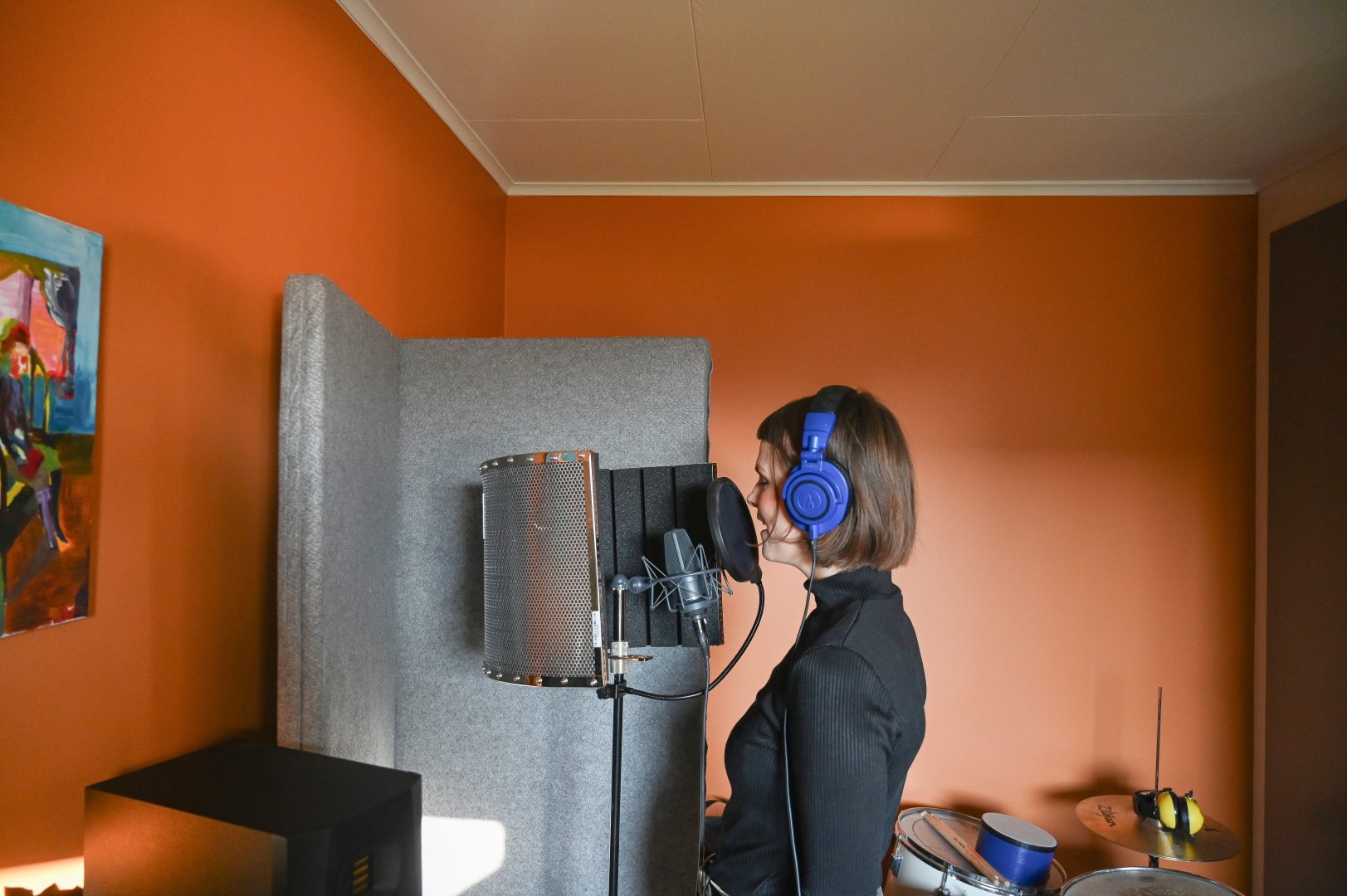 en person i en svart tröja sjunger i en mikrofon i en musikstudio med orange färg på väggarna. 