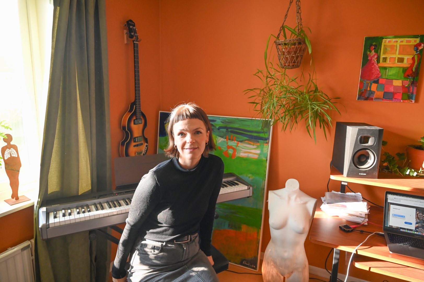 Motivet är en kvinna med kort brunt hår som sitter på en pianostol, i bakgrunden syns en gitarr och ett piano samt tavlor och en växt som hänger på väggen