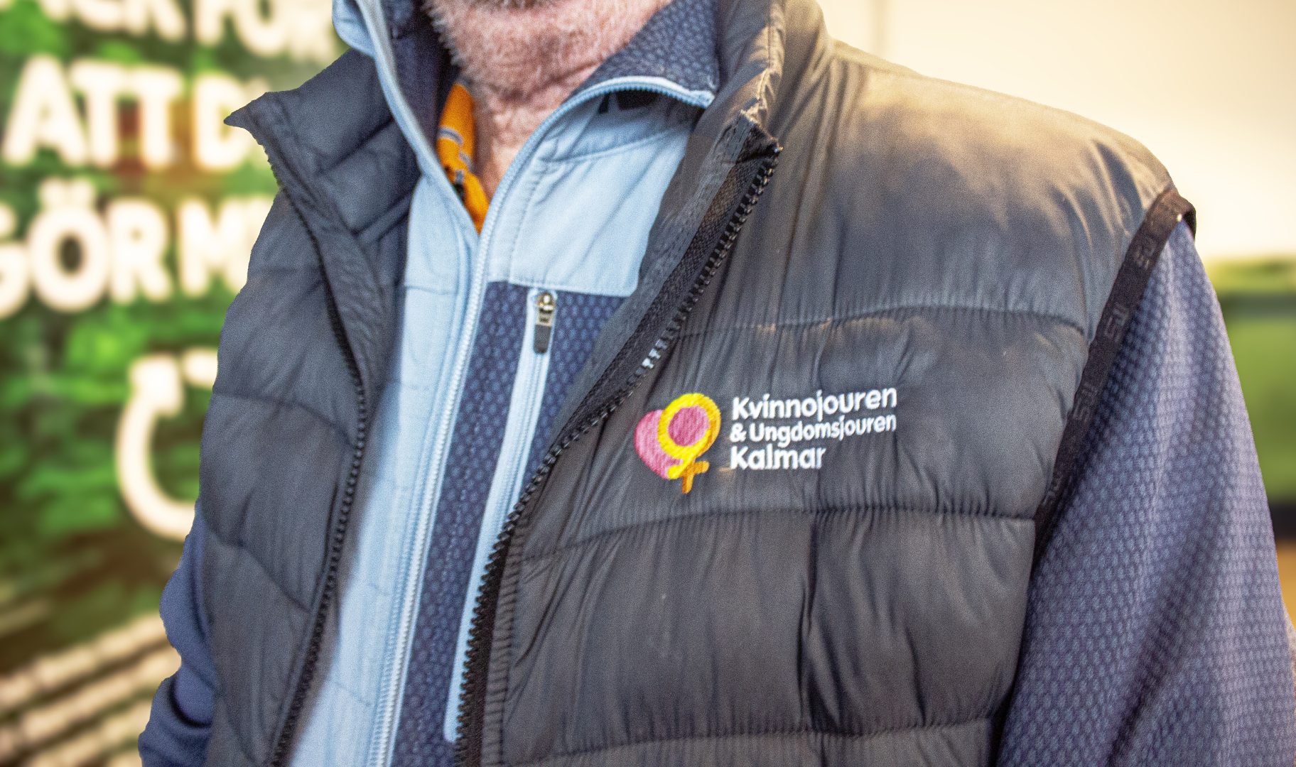 Kåre Eriksson (ansiktet syns ej) med grå väst med texten "kvinnojouren & Ungdomsjouren Kalmar" på bröstet på vänster sida. Foto: Juwelia Jansson