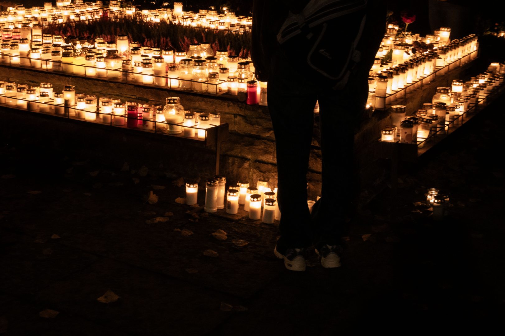 En mörk siluett som står framför minneslunden som är upplyst av en massa ljus.