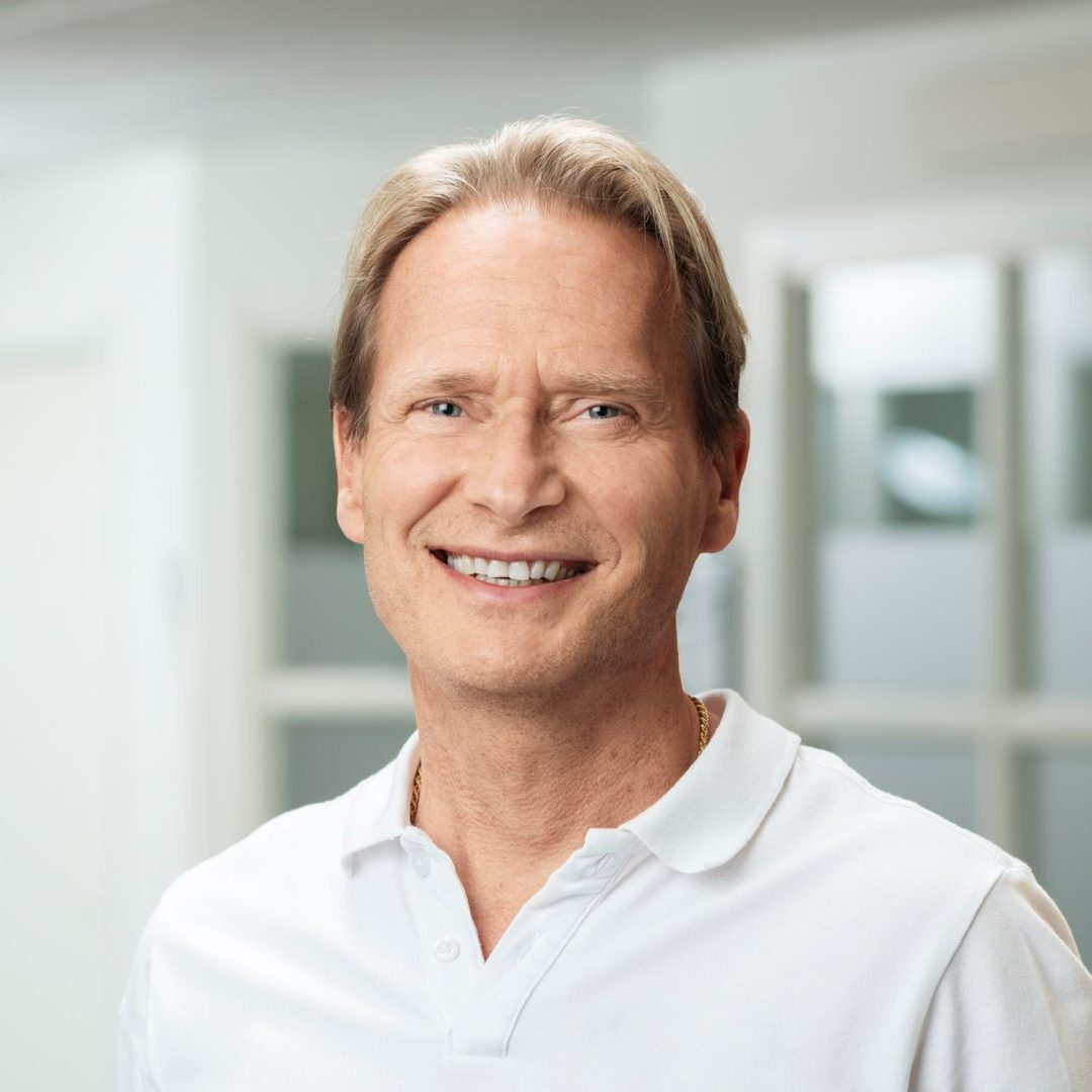 Porträtt av Stefan Regebro, skolchef på Kalmarsunds gymnasieförbund, stående inomhus med vit bakrund. Han tittar mot kameran och ler.
