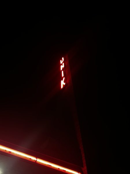 Röda ledlampor utanför UNIK. En röd lampslinga sträcker sig utmed taket och även skylten är upplyst med röda lampor.